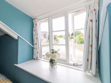 A white window with floral curtains and a vase of white flowers on the windowsill at Alices Cottage in Burton Bradstock