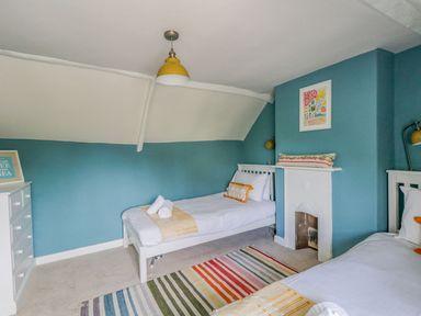 A bedroom with two single beds a striped rug and a white chest of drawers at Alices Cottage in Burton Bradstock