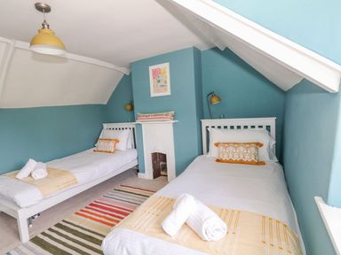 A bedroom with two single beds blue walls yellow lamps and a striped rug at Alices Cottage in Burton Bradstock