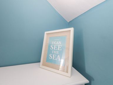 A framed picture with text on a white surface against blue walls at Alices Cottage in Burton Bradstock