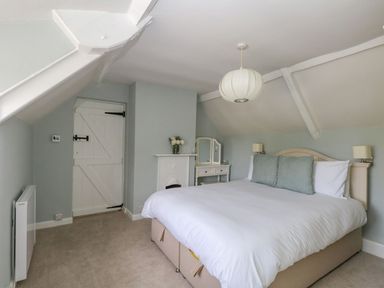 A bedroom with a double bed a dressing table flowers on a mantelpiece and a door at Alice's Cottage in Burton Bradstock