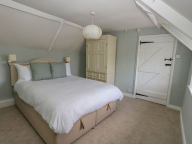 A bedroom with a double bed two pillows a wardrobe and a white door at Alices Cottage in Burton Bradstock