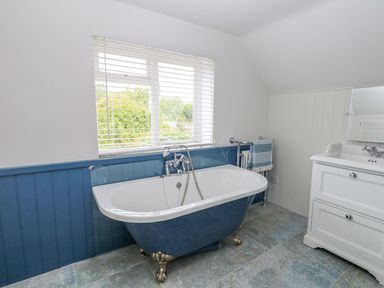 A bathroom with a blue clawfoot bathtub under a window and a white sink cabinet at Alices Cottage in Burton Bradstock