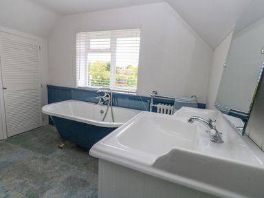 A bathroom with a freestanding bathtub a sink and a window with blinds at Alices Cottage in Burton Bradstock