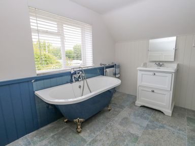 A bathroom with a clawfoot bathtub under a window and a sink with a mirror at Alices Cottage in Burton Bradstock