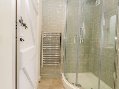 A bathroom with a glass shower enclosure a towel radiator and tiled walls at Alices Cottage in Burton Bradstock