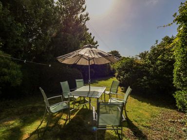 A garden with a table and six chairs under a large umbrella surrounded by bushes at Alices Cottage in Burton Bradstock
