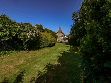 A garden with lawn chairs and table surrounded by bushes and a stone house in the background at Alices Cottage in Burton Bradstock