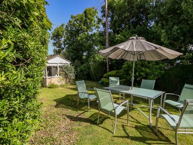 A garden with a glass table and six chairs under a large umbrella near a small shed at Alices Cottage in Burton Bradstock