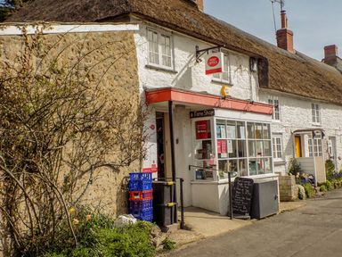 A post office and farm shop in a white stone building with a thatched roof at Alices Cottage in Burton Bradstock