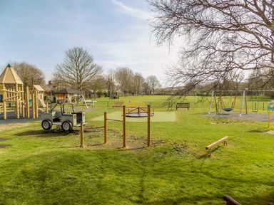 A playground with climbing structures a toy car a merry-go-round and swings at Alices Cottage in Burton Bradstock