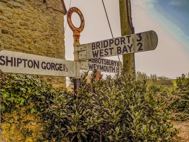 A road signpost with directions to Bridport West Bay Shipton Gorge Abbotsbury and Weymouth in a rural area
