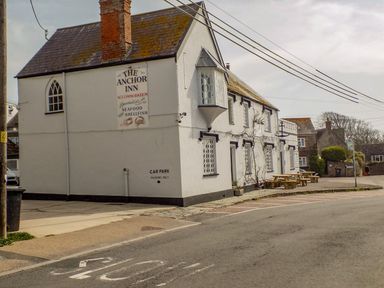 The exterior of a building with a sign for The Anchor Inn and outdoor benches along a street at Alice's Cottage in Burton Bradstock