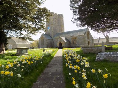 A stone church with a clock tower and yellow flowers along a pathway at Alice's Cottage in Burton Bradstock