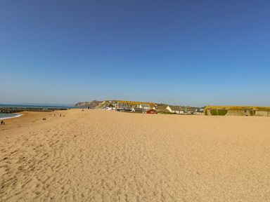 A sandy beach with scattered people near buildings and a sea wall under a clear sky at Alices Cottage in Burton Bradstock