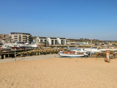 A harbor with boats docked beside buildings and a gravel area in the foreground at Alices Cottage in Burton Bradstock