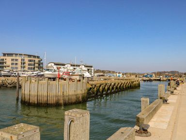A harbor with boats docked near wooden piers and buildings in the background at Alice's Cottage in Burton Bradstock
