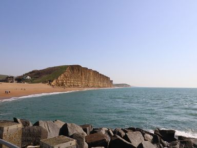 A beach with cliffs and ocean with rocks in the foreground at Alice's Cottage in Burton Bradstock