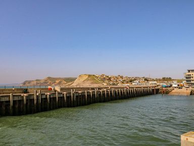 A harbor with boats and a wooden pier with hills and houses in the background at Alices Cottage in Burton Bradstock