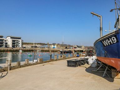 A harbor with boats docked and buildings along the water at Alice's Cottage in Burton Bradstock
