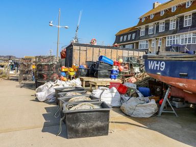 A harbor area with fishing equipment crates and a boat near large buildings at Alices Cottage in Burton Bradstock