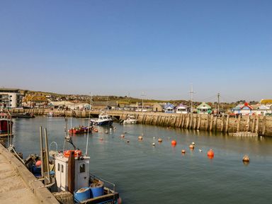A harbor with boats on water and small colorful huts along the pier at Alice's Cottage in Burton Bradstock