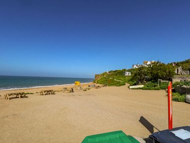 A beach with picnic tables and a sandy shore near houses on a hill at Alices Cottage in Burton Bradstock