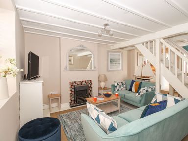 A living room with two teal sofas a wooden coffee table a fireplace and a television at Little Gull Cottage in Weymouth