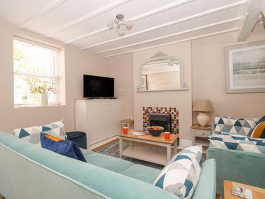 A living room with two sofas a coffee table a TV on a cabinet a mirror above a fireplace and a window with flowers at Little Gull Cottage in Weymouth