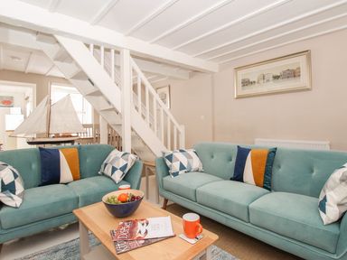 A living room with two teal sofas and a coffee table with fruit bowl and mugs at Little Gull Cottage in Weymouth