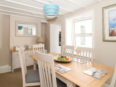 A dining room with a wooden table and chairs a sideboard with a lamp and radio and a window at Little Gull Cottage in Weymouth