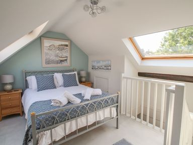 A bedroom with a double bed blue and white bedding two bedside tables lamps and a skylight window at Little Gull Cottage in Weymouth