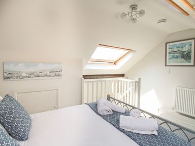 A bedroom with a bed and folded towels near a window and framed pictures on the walls at Little Gull Cottage in Weymouth