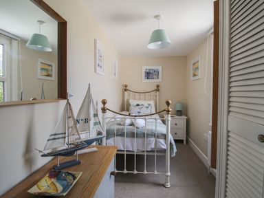 A bedroom with a single bed and nautical decorations including a sailboat model and framed pictures at Little Gull Cottage in Weymouth