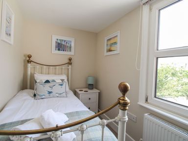 A small bedroom with a single bed with white and blue bedding a bedside table with a lamp and framed pictures on the wall at Little Gull Cottage in Weymouth