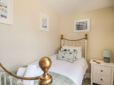 A small bedroom with a single bed a nightstand with a lamp and framed pictures on the walls at Little Gull Cottage in Weymouth