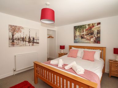 A bedroom with a wooden bed and two bedside tables with lamps and paintings on the walls at Little Gull Cottage in Weymouth