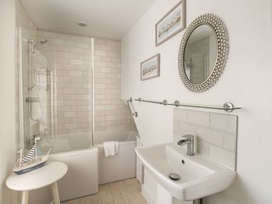 A bathroom with a bathtub shower combination sink round mirror and a small table with a model sailboat at Little Gull Cottage in Weymouth