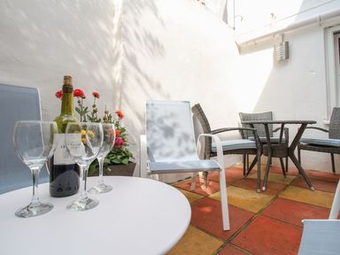A small outdoor patio with tiled floor four chairs a table a bottle of wine and three wine glasses Little Gull Cottage Weymouth