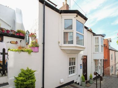 A white exterior house with bay windows and potted plants on a sloped street at Little Gull Cottage in Weymouth