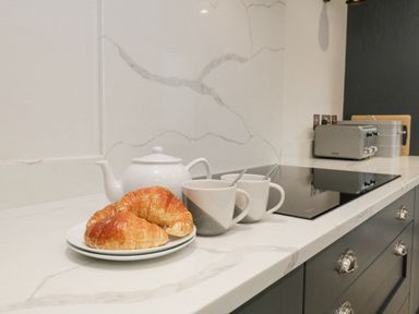 A kitchen countertop with a teapot two mugs and croissants near an induction stove at Forty Five in Keswick