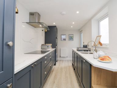 A galley kitchen with blue cabinets white countertops and light wood flooring at Forty Five in Keswick