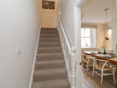 A stairway with beige carpet leading up next to a dining room with a wooden table set with plates and chairs at Forty Five in Keswick