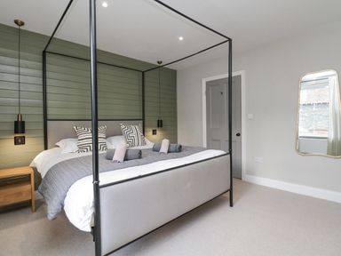A bedroom with a four-poster bed, two bedside tables with hanging pendant lights, a door, and a wall mirror at Forty Five in Keswick