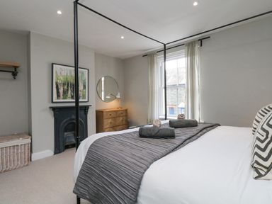 A bedroom with a four-poster bed a chest of drawers a round mirror and a fireplace at Forty Five in Keswick