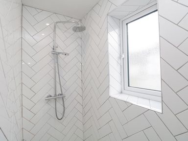 A shower area with wall-mounted showerhead and window in a tiled bathroom at Forty Five in Keswick