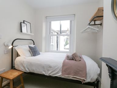 A small bedroom with a single bed by a window a wooden stool and a wall-mounted shelf with coat hangers at Forty Five in Keswick
