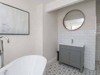 A bathroom with a freestanding bathtub a gray vanity with a sink and round mirror above it and a picture of flamingos on the wall at Forty Five in Keswick