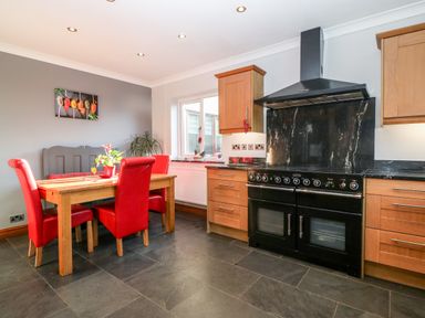 A kitchen with wooden cabinets a black stove and a dining table with red chairs at Tyn Rallt Ice Cream Farm Malltraeth near Newborough