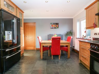 A kitchen with a wooden dining table and red chairs a black refrigerator wooden cabinets and a window at Tyn Rallt Ice Cream Farm Malltraeth near Newborough